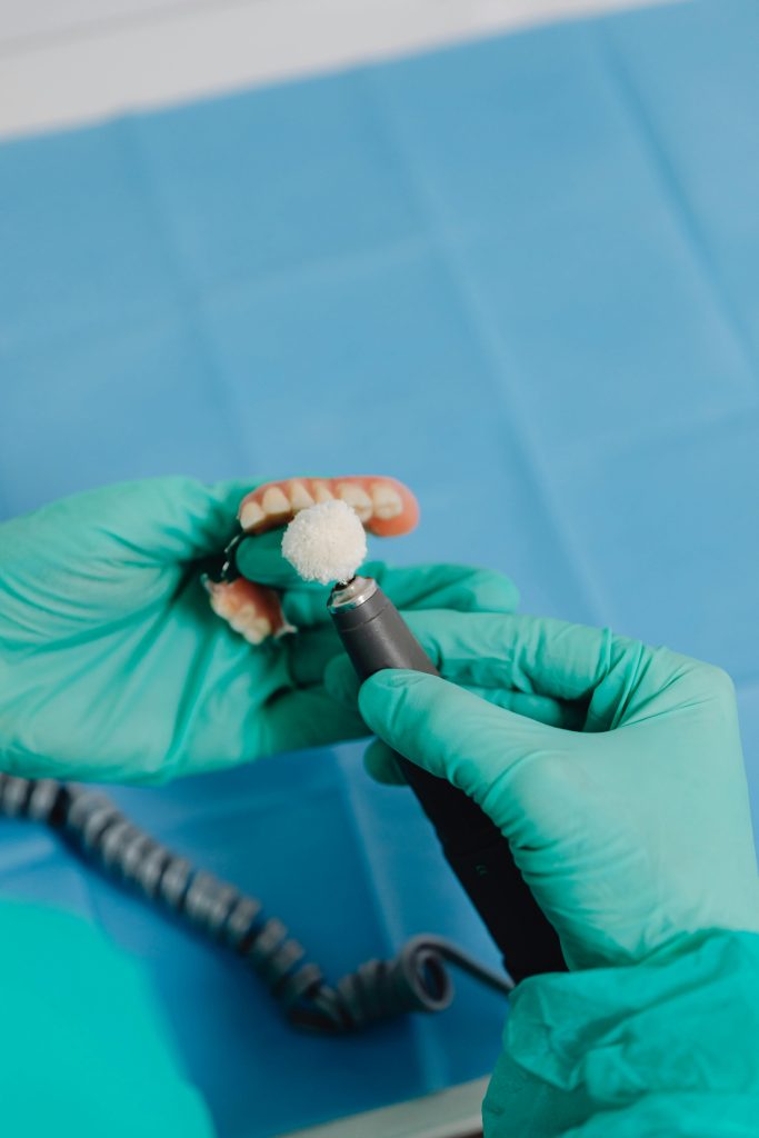 Dentist polishing a denture with green latex gloves. Dental care and hygiene concepts.
