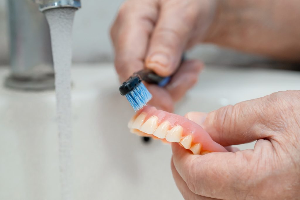 Person cleaning a lower denture with a soft denture brush at home